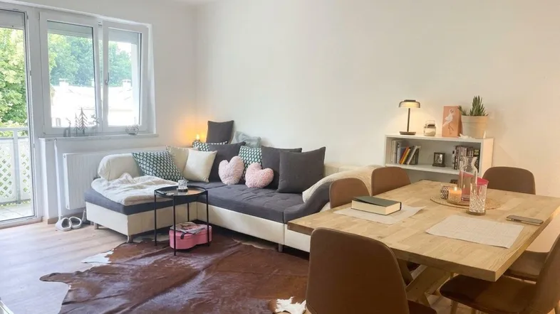 Helles Wohn- und Esszimmer mit Ecksofa, Holzboden und Zugang zum Balkon.