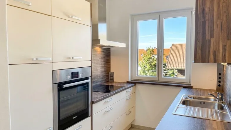 Moderne Einbauküche mit hellen Fronten, integriertem Backofen und Blick ins Grüne.
