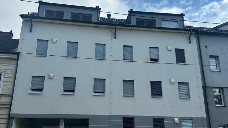 Mehrstöckiges Wohngebäude mit moderner Fassade, Rollläden und Dachgauben an einer Straße gelegen.