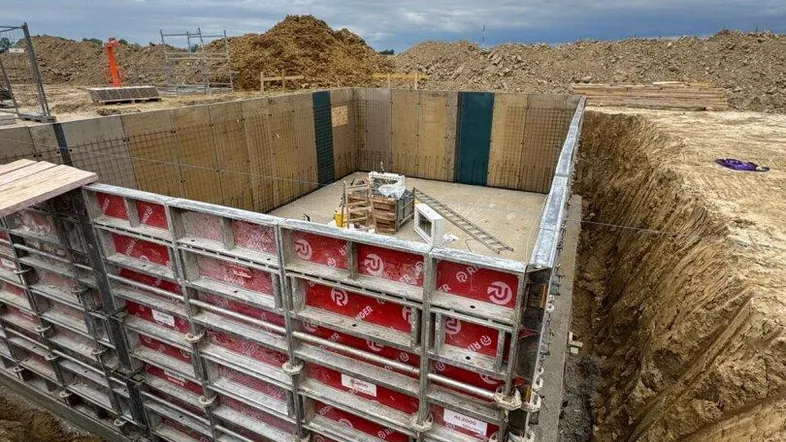 Baugrube mit Schalung für das Fundament eines Neubaus unter bewölktem Himmel.