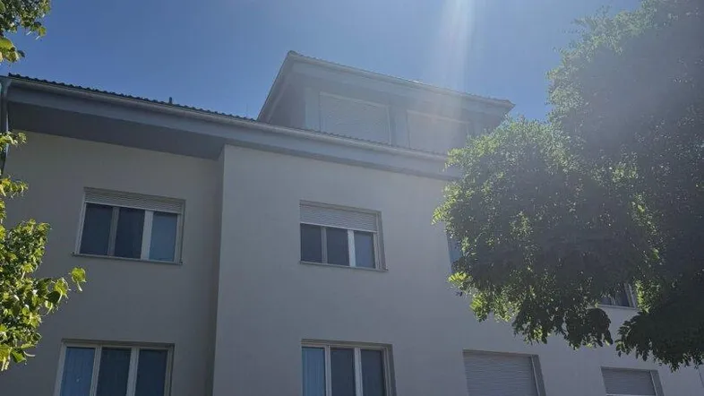 Fassade eines modernen Mehrfamilienhauses mit Tiefgaragenzufahrt unter strahlendem Sonnenschein.