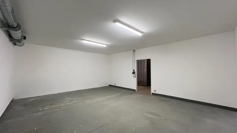 Geräumiger, leerer Lagerraum mit Betonboden und sichtbaren Rohren an der Decke und Wänden.
