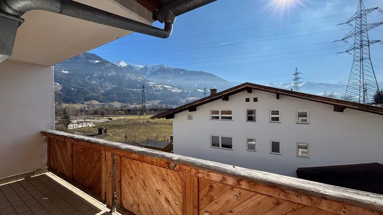 Sonniger Balkon mit Holzbalkonbrüstung und weitem Blick auf die umliegende Berglandschaft.