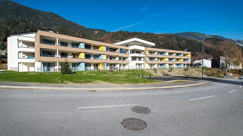 Modernes Apartmentgebäude mit mehreren Balkonen und Bergblick in alpiner Umgebung.