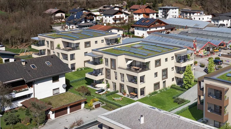 Luftaufnahme von modernen Wohngebäuden mit Gründächern und Solaranlagen in bergiger Umgebung.