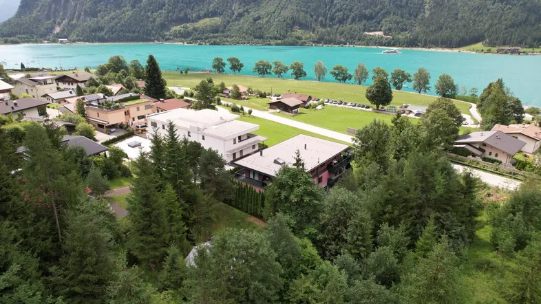 Luftaufnahme eines Dorfes am türkisfarbenen See, umgeben von Bergen und üppiger Vegetation.