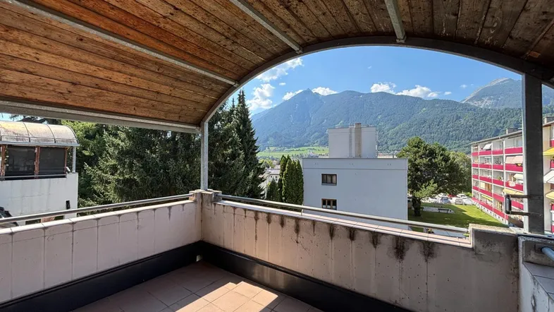 Geräumiger Balkon mit Holzdach und einem weiten Blick auf die umliegende Berglandschaft und viel Grün.