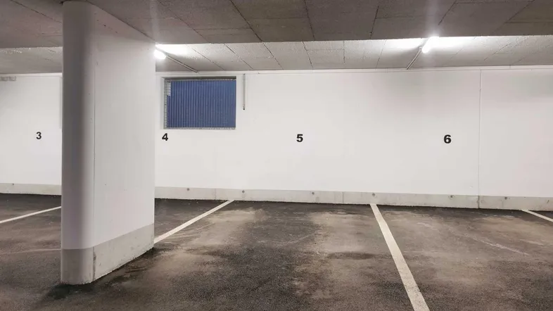 Tiefgarage mit nummerierten Stellplätzen, sauberem Betonboden und einem kleinen Fenster.