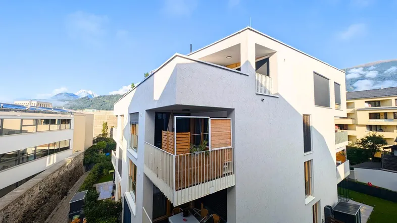Modernes Wohngebäude mit mehreren Balkonen und Bergblick unter blauem Himmel.