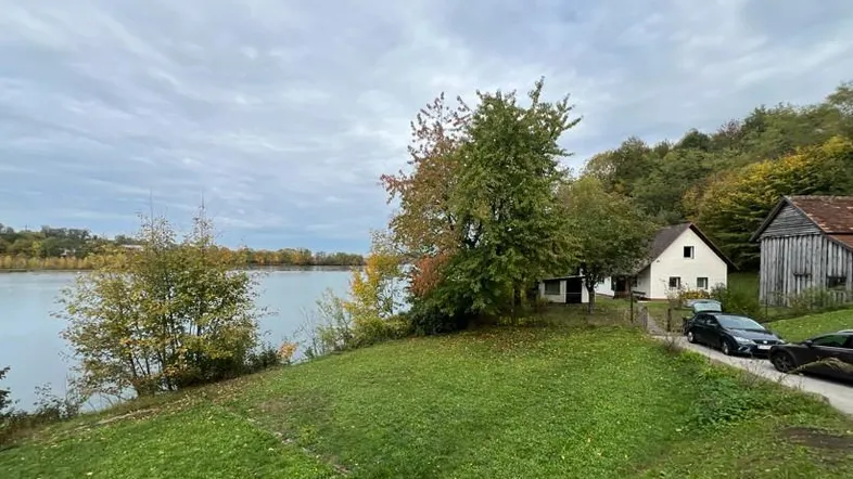 Blick auf das Anwesen mit einem Haus, Nebengebäuden und einem See im Hintergrund unter bewölktem Himmel.