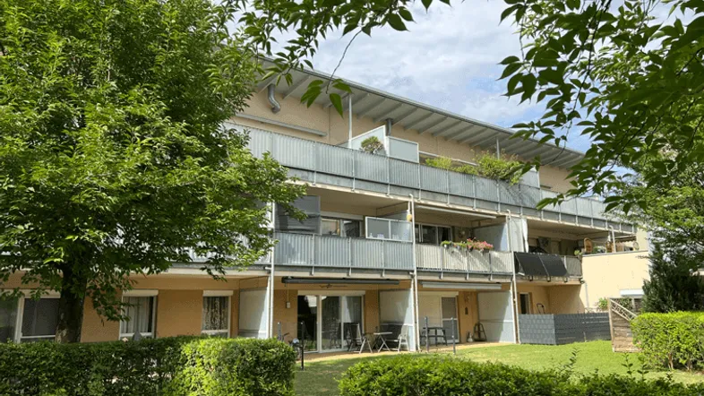 Rückseite eines Wohngebäudes mit Balkonen, Terrassen und gepflegtem Gemeinschaftsgarten.