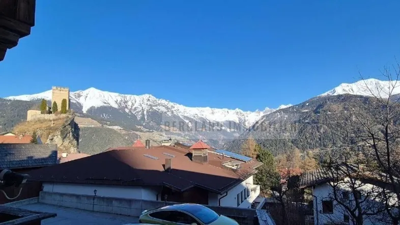 Panoramablick auf schneebedeckte Berge und eine historische Burg unter strahlend blauem Himmel.