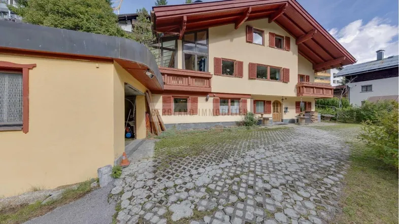 Traditionelles Haus mit alpiner Architektur, Holzdetails, Fensterläden und einer gepflasterten Auffahrt.