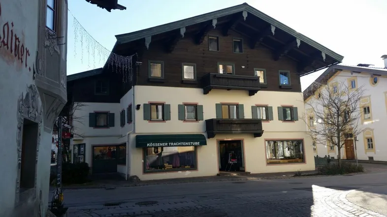 Traditionelles Gebäude im alpenländischen Stil mit dunklem Holz und hellen Fassaden, im Erdgeschoss befinden sich Geschäfte.