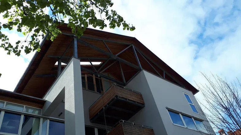 Moderne Architektur mit markantem Holzdach, großen Fenstern und kleinen Balkonen unter blauem Himmel.
