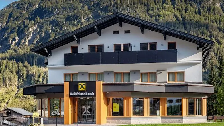 Modernes Gebäude mit Balkonen und großen Fenstern, umgeben von einer Berglandschaft.