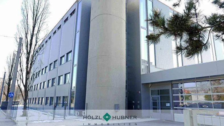 Moderne Außenansicht eines Geschäftsgebäudes mit markanter Betonsäule und großen Glasflächen.
