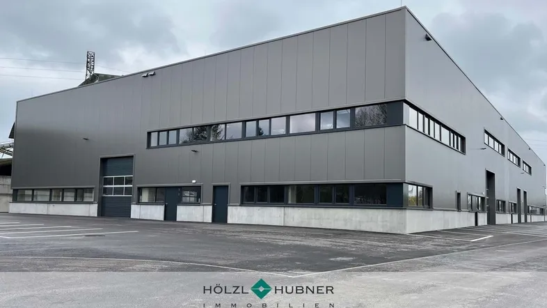Moderne Gewerbeimmobilie mit grauer Fassade, großen Fenstern und einem geräumigen Parkplatzbereich.