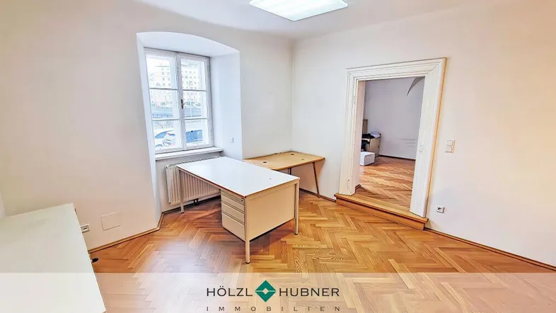 Helles Büro mit Fischgrätparkett, weißen Wänden und einem Fenster, das Tageslicht hereinlässt.