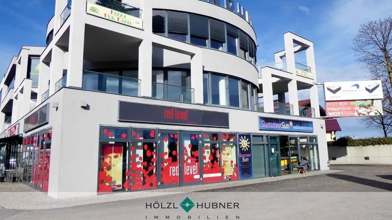 Modernes Geschäftsgebäude mit runder Architektur, großen Glasflächen und verschiedenen Ladenlokalen.