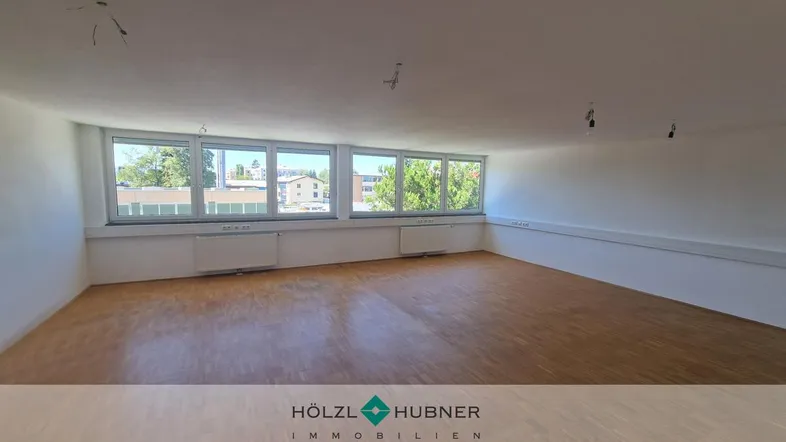 Geräumiger Büroraum mit großen Fenstern, die viel Tageslicht hereinlassen und einen Blick ins Grüne bieten.