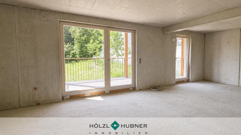 Unfertiger Innenraum mit großen Fenstern und Zugang zu einem Balkon, der viel natürliches Licht hereinlässt.