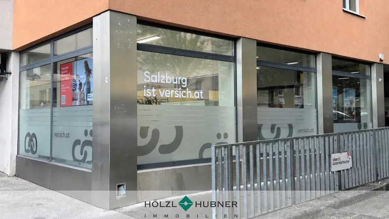 Eingangsbereich eines Geschäftsgebäudes mit großen Fenstern und einer Rampe für Barrierefreiheit.