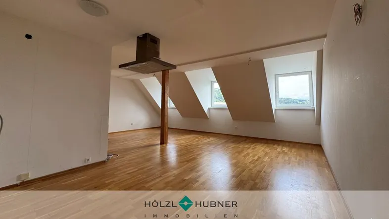 Geräumiger offener Wohnbereich mit Holzboden, Dachschrägen und mehreren Fenstern, bereit für die Einrichtung.