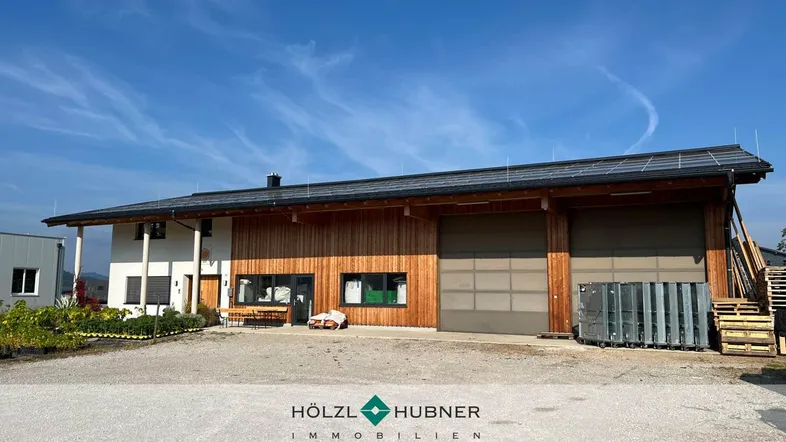 Modernes Gebäude mit Holzfassade, großen Garagentoren und Photovoltaikanlage auf dem Dach.
