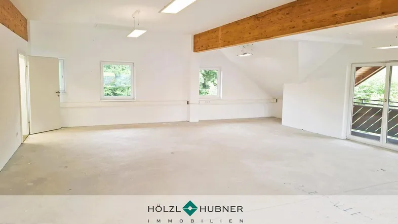 Geräumiger, heller Innenraum mit sichtbaren Holzbalken und großen Fenstern, bereit für den Ausbau.