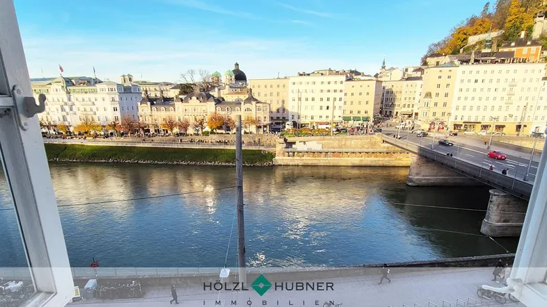 Panoramablick auf die Salzach und die historische Altstadt von Salzburg durch ein geöffnetes Fenster.
