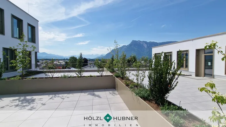 Geräumige Dachterrasse mit modernen Fliesen, begrünten Hochbeeten und einem weiten Blick auf die Berge und die Stadt.