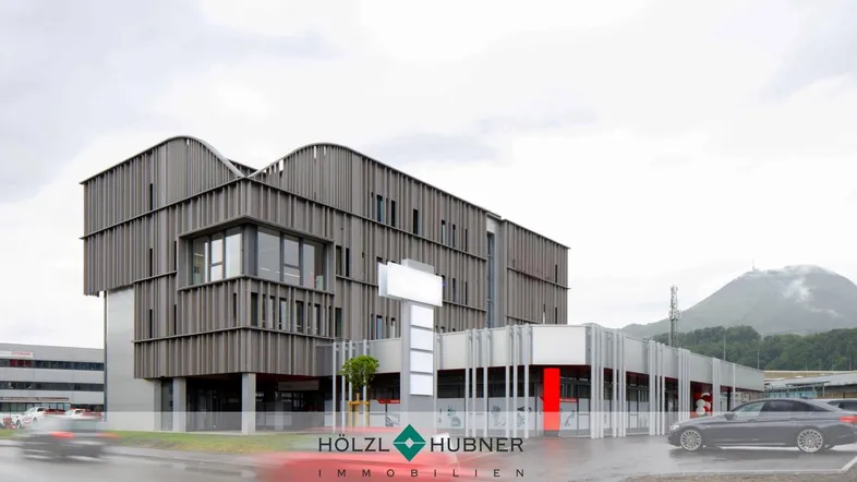 Modernes Geschäftsgebäude mit markanter Holzfassade und Bergkulisse im Hintergrund, umgeben von Parkplätzen.