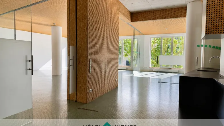 Geräumiger, moderner Büroraum mit großen Fenstern, Glaswänden und einer kleinen Küchenzeile.