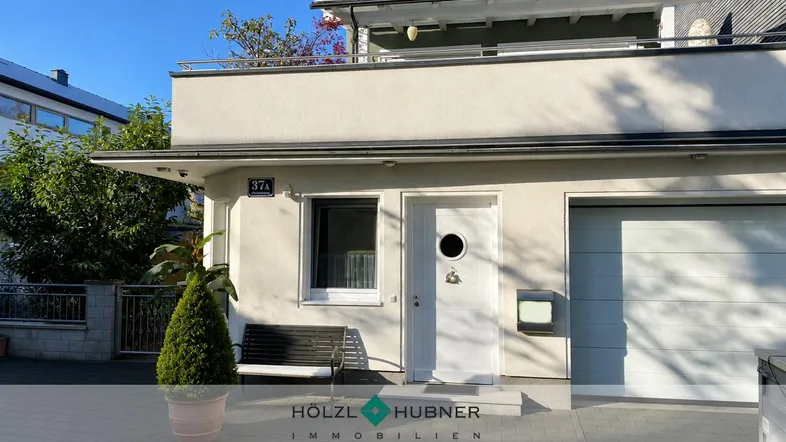Eingangsbereich eines modernen Gebäudes mit Garage und kleinem Balkon im Obergeschoss.