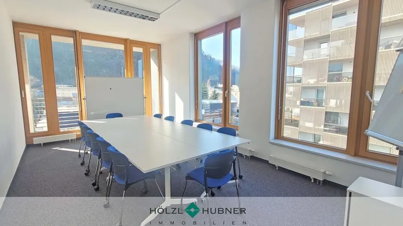 Heller Konferenzraum mit großen Fenstern, Teppichboden und Blick auf die Umgebung und Berge.