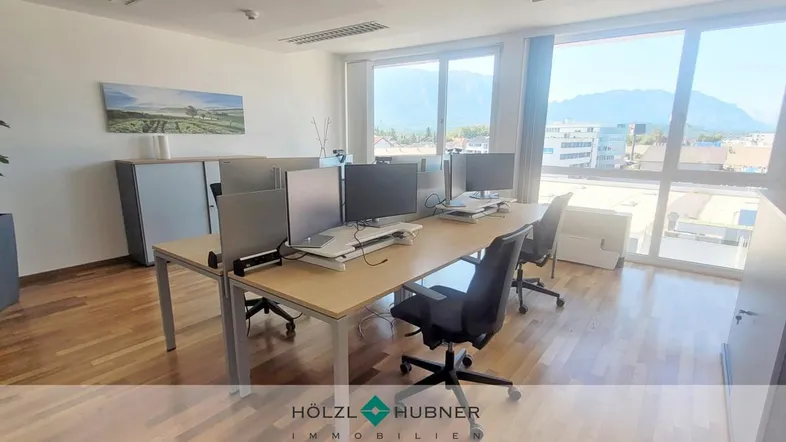 Modernes Büro mit mehreren Arbeitsplätzen, Holzboden und großen Fenstern mit Bergblick.