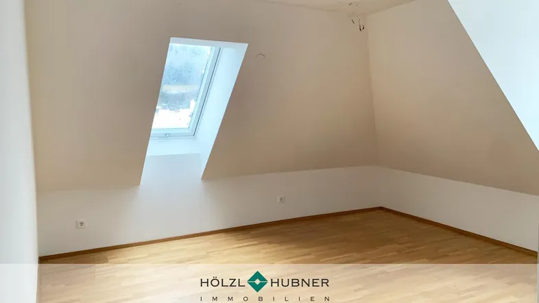 Helles Zimmer im Dachgeschoss mit schrägen Wänden und einem Dachfenster, bereit zur Einrichtung.
