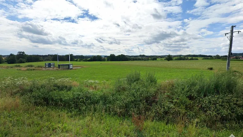 Weite grüne Landschaft mit Feldern und einem kleinen Gebäude unter bewölktem Himmel, typisch für ländliche Gegenden.