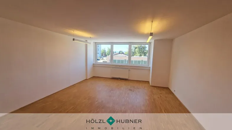 Heller, leerer Raum mit Holzboden und großen Fenstern, ideal als Büro oder vielseitiger Wohnbereich.