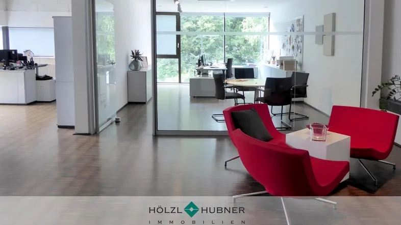 Moderner Bürobereich mit Holzboden, Glaswänden und roten Loungesesseln, bietet eine helle und offene Arbeitsumgebung.