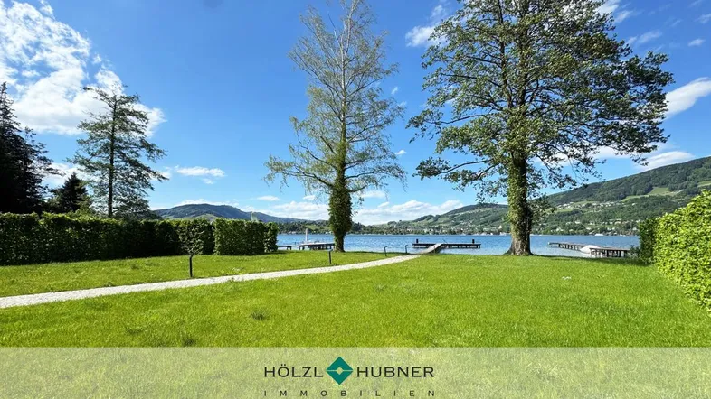 Grüner Gartenbereich mit direktem Zugang zum See und Bergblick unter blauem Himmel.
