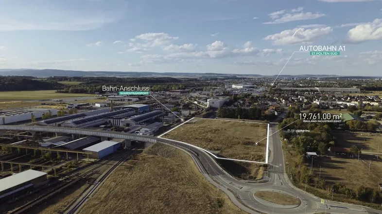 Luftaufnahme eines großen Grundstücks in einem Industriegebiet mit Autobahn- und Bahnanschluss in der Ferne.