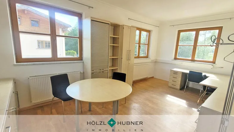 Heller Büroraum mit Holzboden, großen Fenstern und funktionalen Büromöbeln, ideal für produktives Arbeiten.