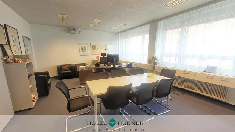 Geräumiges Büro mit Konferenztisch, Teppichboden und großen Fenstern, die viel Tageslicht hereinlassen.
