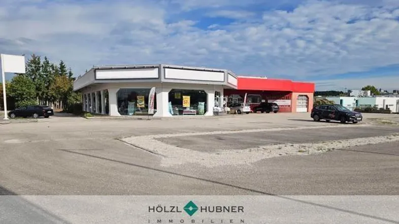 Gewerbegebäude mit großer Glasfassade und weitläufigem Parkplatz unter bewölktem Himmel.