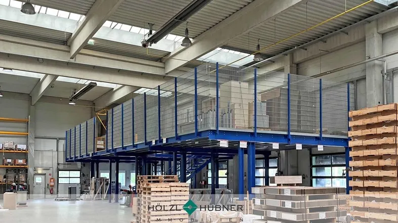Geräumige Lagerhalle mit hoher Decke, Zwischengeschoss und natürlichem Lichteinfall durch Oberlichter.