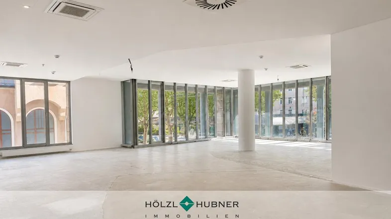 Großzügige, leere Bürofläche mit vielen Fenstern, weißen Wänden und Betonboden.