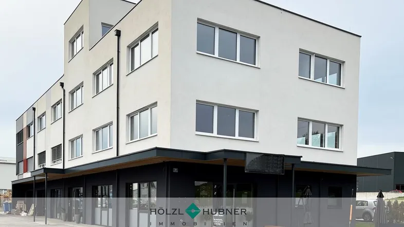 Modernes Gebäude mit weißer und dunkelgrauer Fassade, großen Fenstern und einem Geschäft im Erdgeschoss.