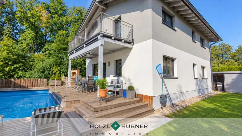 Modernes Haus mit großem Pool, Holzterrasse und möbliertem Außenbereich unter blauem Himmel.